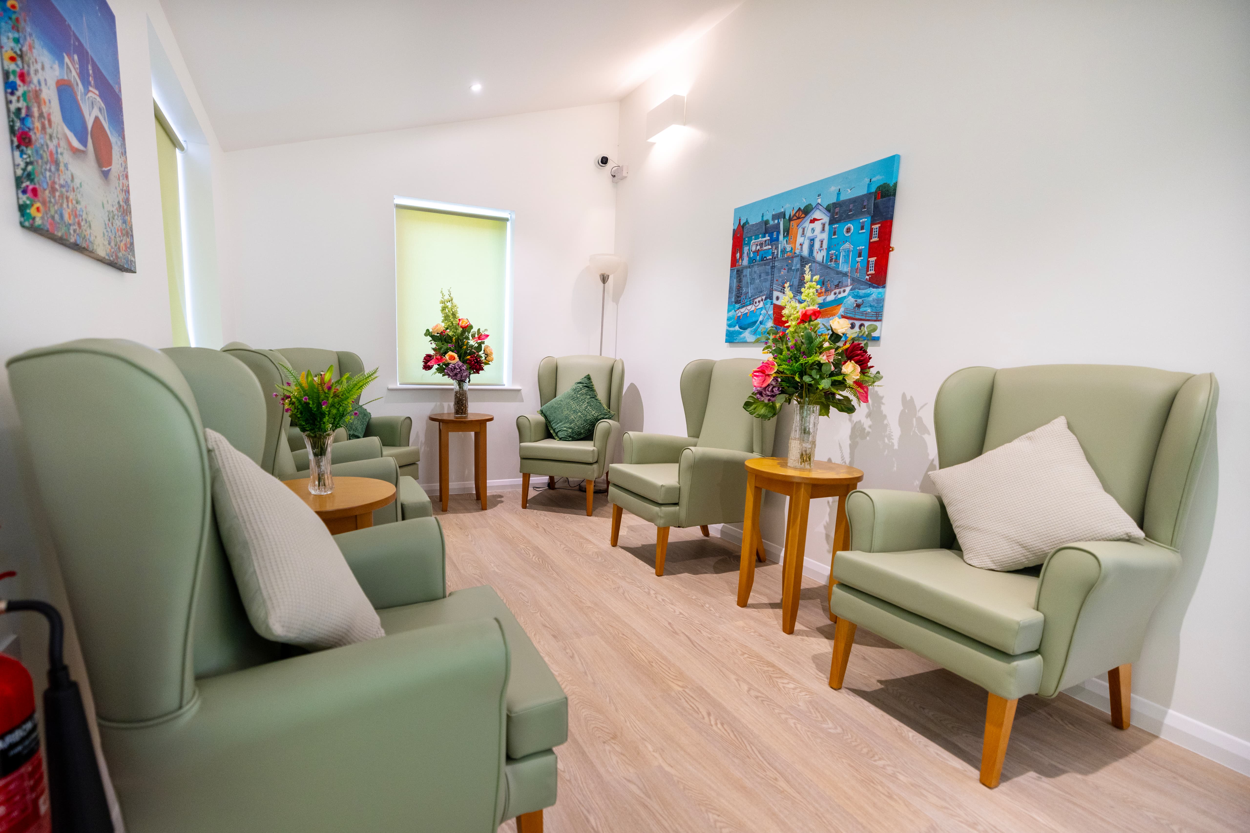 Quiet lounge with sage green chairs and colorful seaside artwork